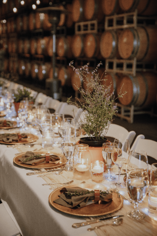 An Oregon winery table setting for a harvest dinner in barrel room. The theme is green and gold with light linens and lots of delicate glassware.