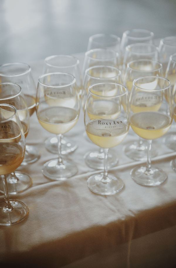 A shot of many glasses of white wine with the logo for RoxyAnn Winery featured on the front of each glass.