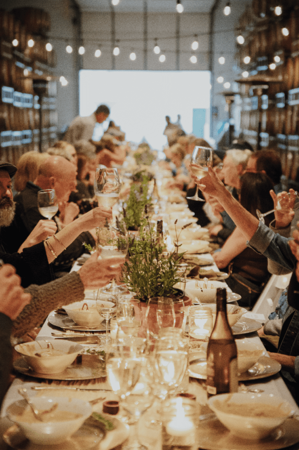 Guests at a long table at an Oregon Winery toasting and clinking glasses of wine.