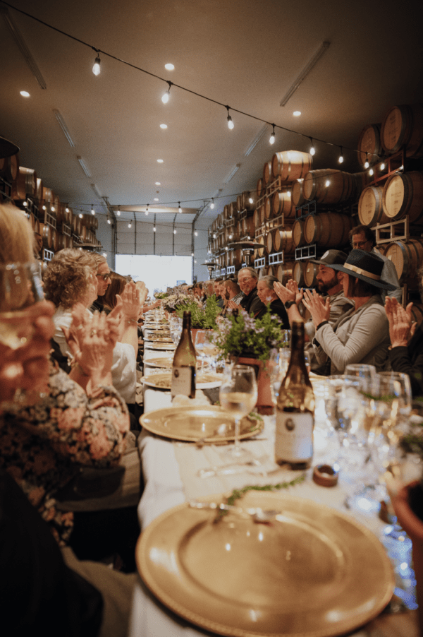 Guests at a long table at an Oregon Winery applauding and enjoying dinner and wine.